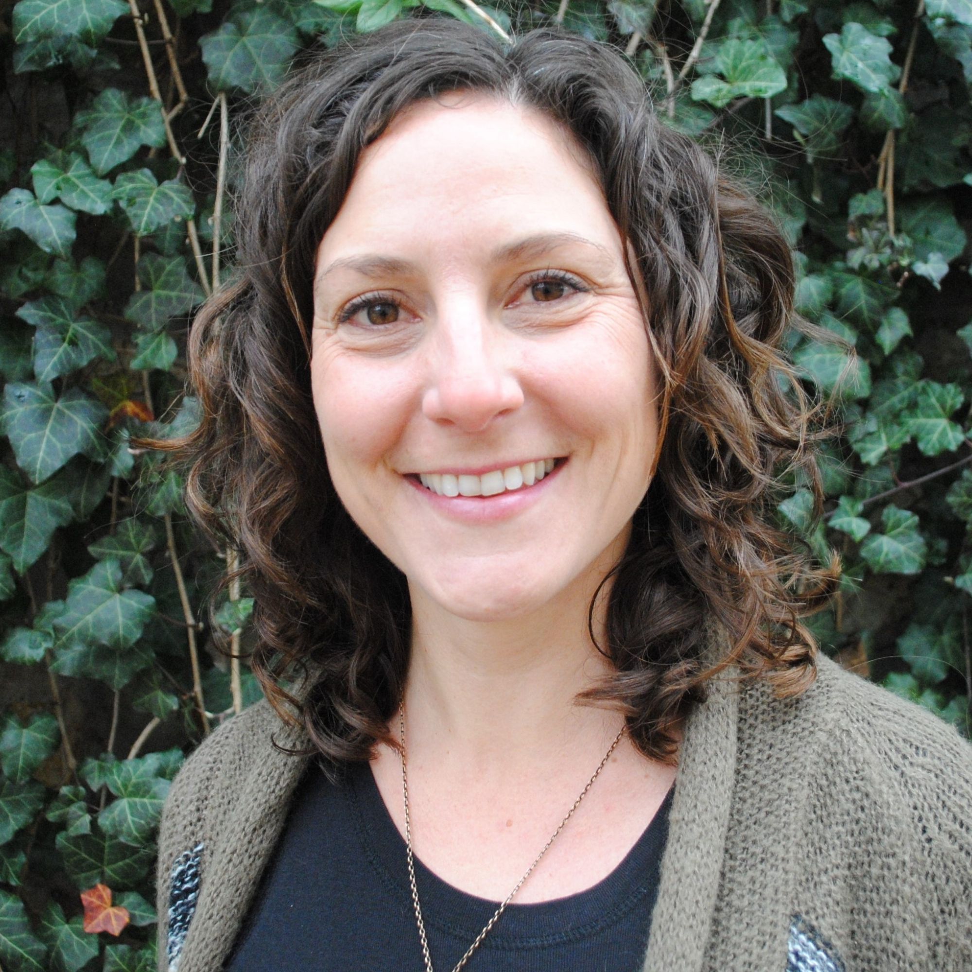 Sarah Dehart Faltico smiling in front of foliage.