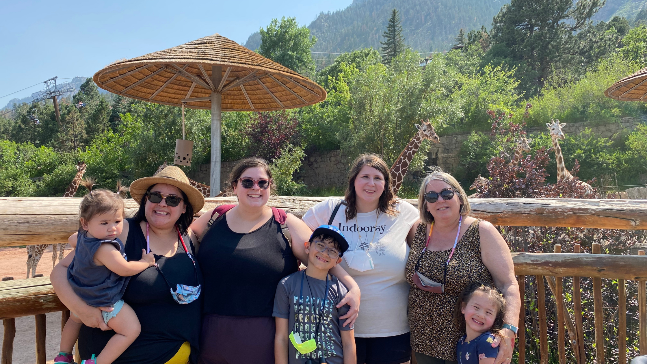 Dorothy Barnett with her three daughters and three grandchildren in front of a giraffe exhibit at a zoo.